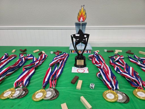 Groups of three medals each surround a black trophy on a green tablecloth