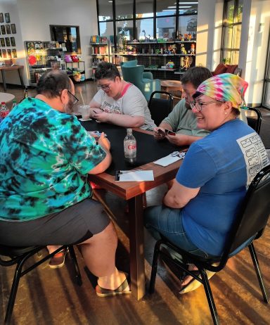 6.3.26 Uno Tournament - Finals Five adults sit around a table playing Uno in a board game cafe