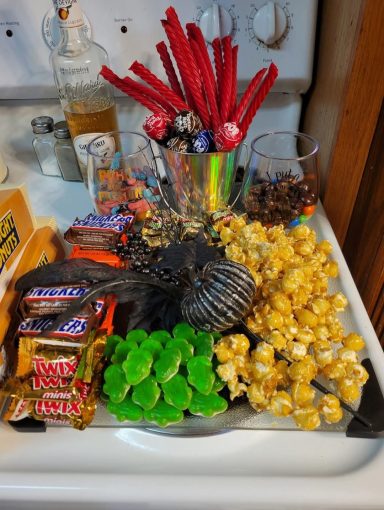 A charcuterie board made out of Halloween candy and caramel corn decorated with a spray of black flowers