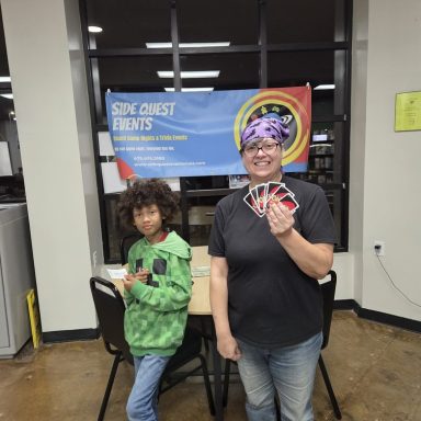 10.7.26 Uno Tournament - Winner A child holding a gift certificate and an adult holding Uno cards stand in front of a blue banner