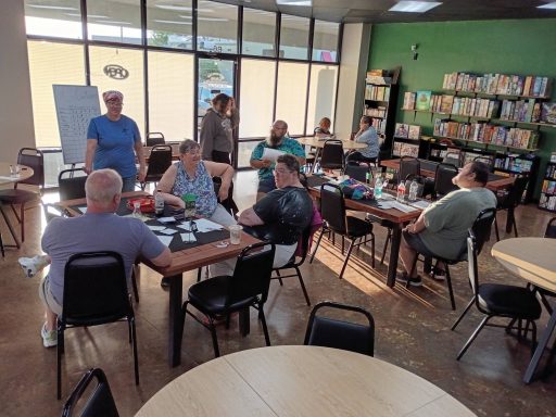 5.14.26 Trivia Night Groups of people sit around tables in front of windows in a board game cafe