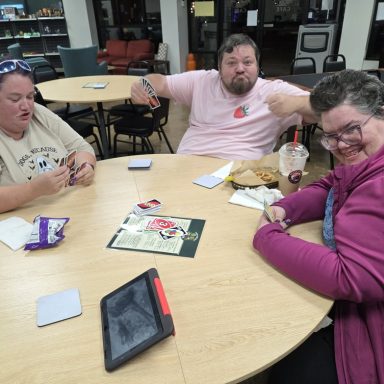 10.7.26 Uno Tournament Three people sit around a table playing Uno