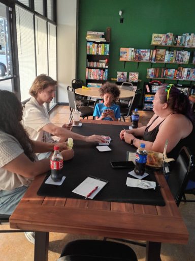 Three adults and a child play Uno in front of a wall of board game shelves