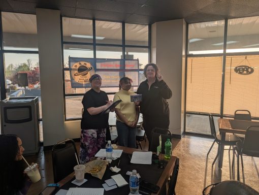 4.9.26 Trivia Night Winners Three people stand in front of windows and a banner