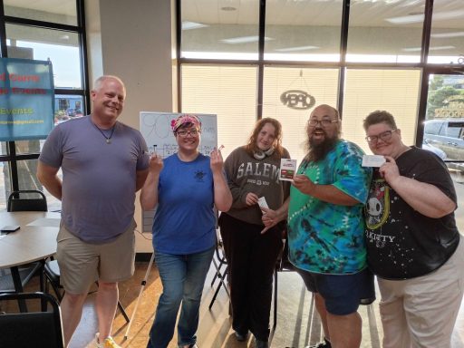 5.14.26 Trivia Night Winners Five people stand in a row in front of a window holding various prizes