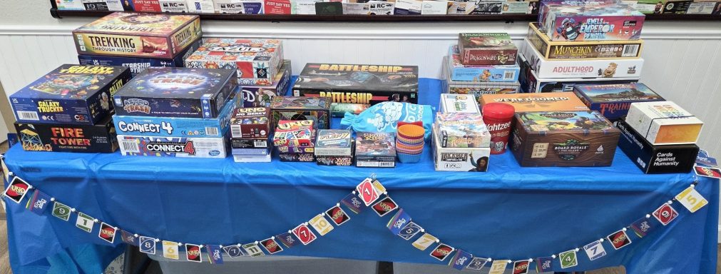 A table with a blue tablecloth covered with board games and decorated with an Uno card garland